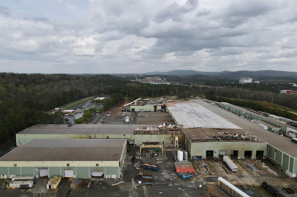 Does My Commercial Property Qualify for Hurricane Damage Claims – Klotzman Law Firm Aerial view of an expansive industrial site featuring several large warehouses, some partially damaged, surrounded by a forested area and distant hills, under a cloudy sky.