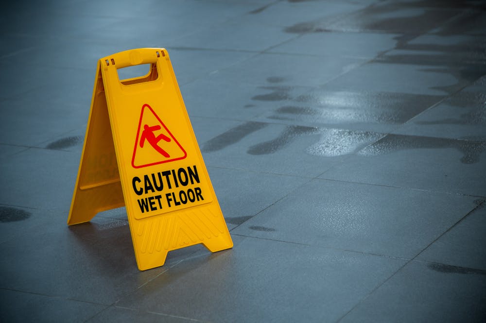 Miami Slip and Fall Accident Statistics – Klotzman Law Firm Yellow caution sign displaying a warning for a wet floor stands on a shiny tiled surface, indicating potential slipping hazards in a well-lit indoor environment.