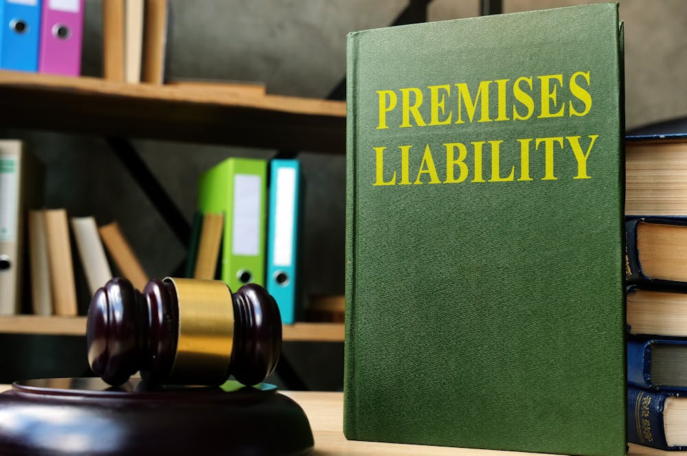 Premises Liability Laws in Florida – Klotzman Law Firm A green book titled "PREMISES LIABILITY" stands upright next to a wooden gavel on a desk, surrounded by colorful binders and shelves filled with books in a law office setting.