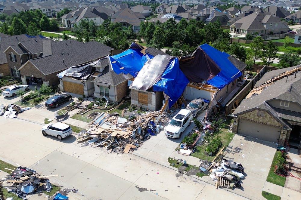 The Impact Recent Hurricanes Had in Sarasota – Klotzman Law Firm A house with significant roof damage is covered with blue tarps, while debris and construction materials are scattered around its front yard; neighboring homes are visible in the background.